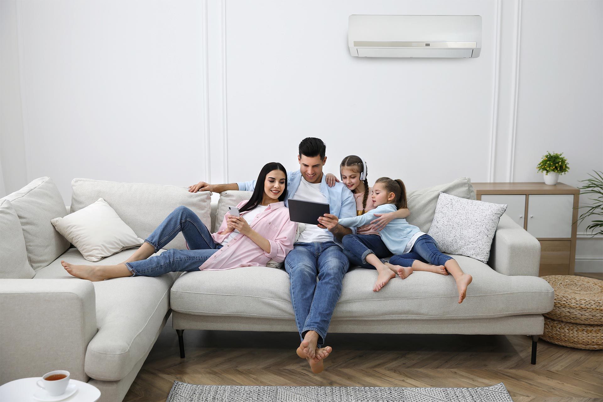 A family is sitting on a couch in a living room looking at a tablet