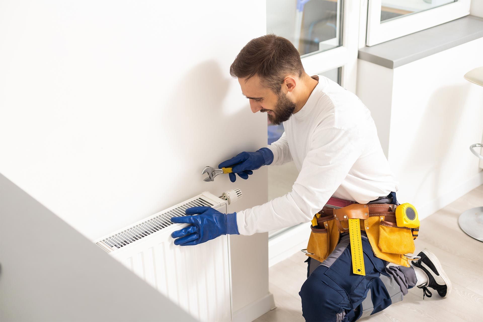 A man is kneeling down fixing a radiator in a room