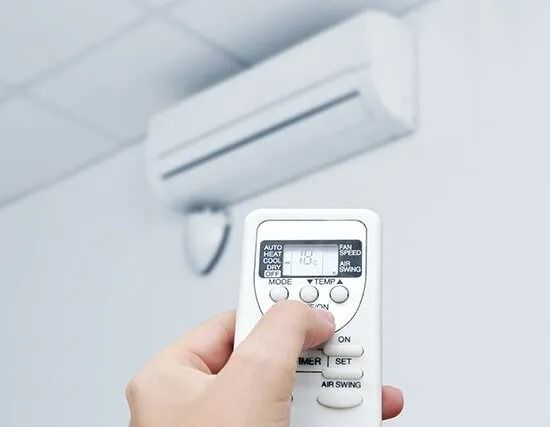A Person is Holding a Remote Control in Front of an Air Conditioner — BJ Heating & Cooling in South Albury, NSW