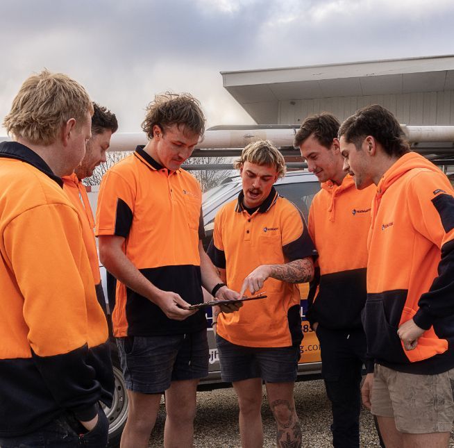 A Group of Men in Orange Shirts Are Looking at a Tablet — BJ Heating & Cooling in South Albury, NSW