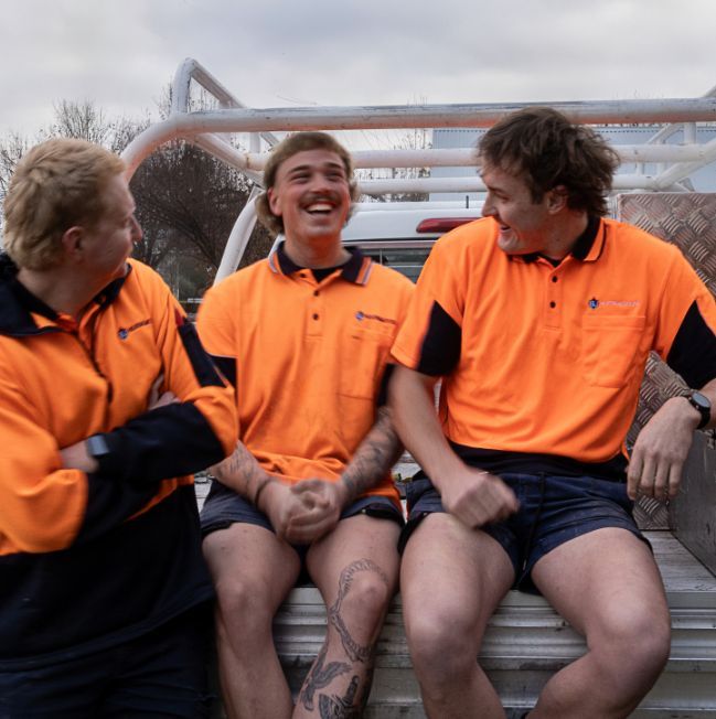 Three Men in Orange Shirts Are Sitting on the Back of a Truck — BJ Heating & Cooling in South Albury, NSW