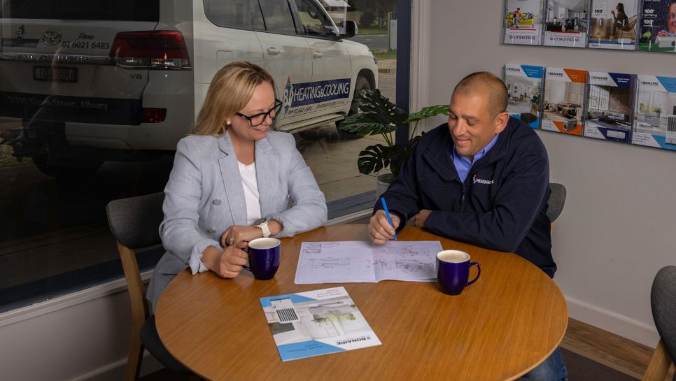 A Man and a Woman Are Sitting at a Table With Cups of Coffee — BJ Heating & Cooling in South Albury, NSW