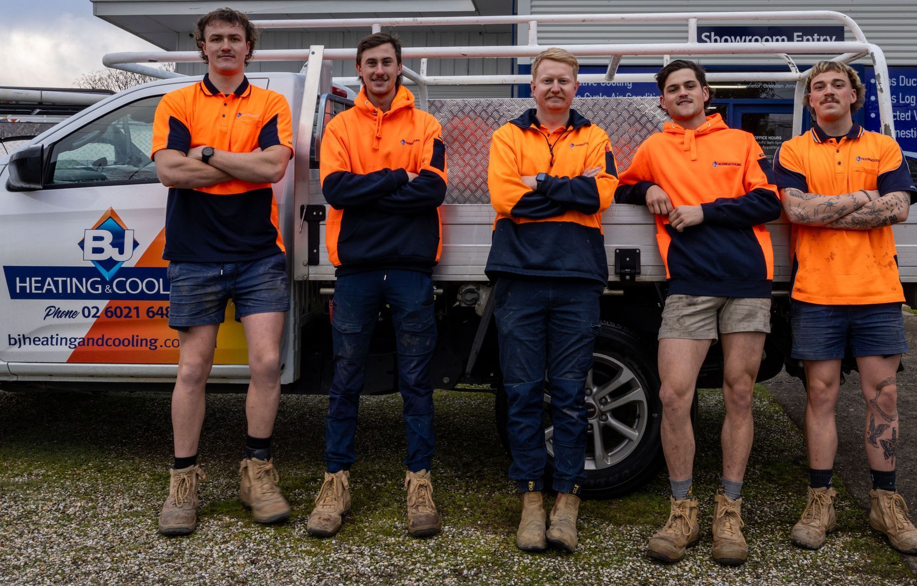 A Group of Men in Orange Shirts Are Looking at a Tablet — BJ Heating & Cooling in South Albury, NSW