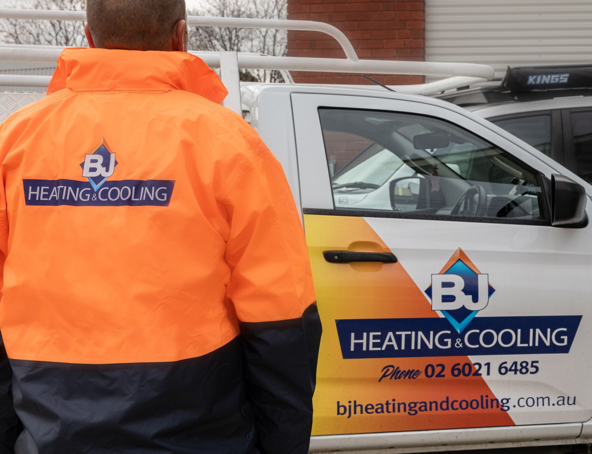 A Man in an orange jacket is walking towards a car — BJ Heating & Cooling in South Albury, NSW