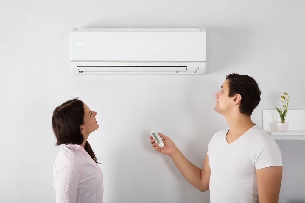 A Man and a Woman Are Standing Next to Each Other in Front of an Air Conditioner — BJ Heating & Cooling in South Albury, NSW