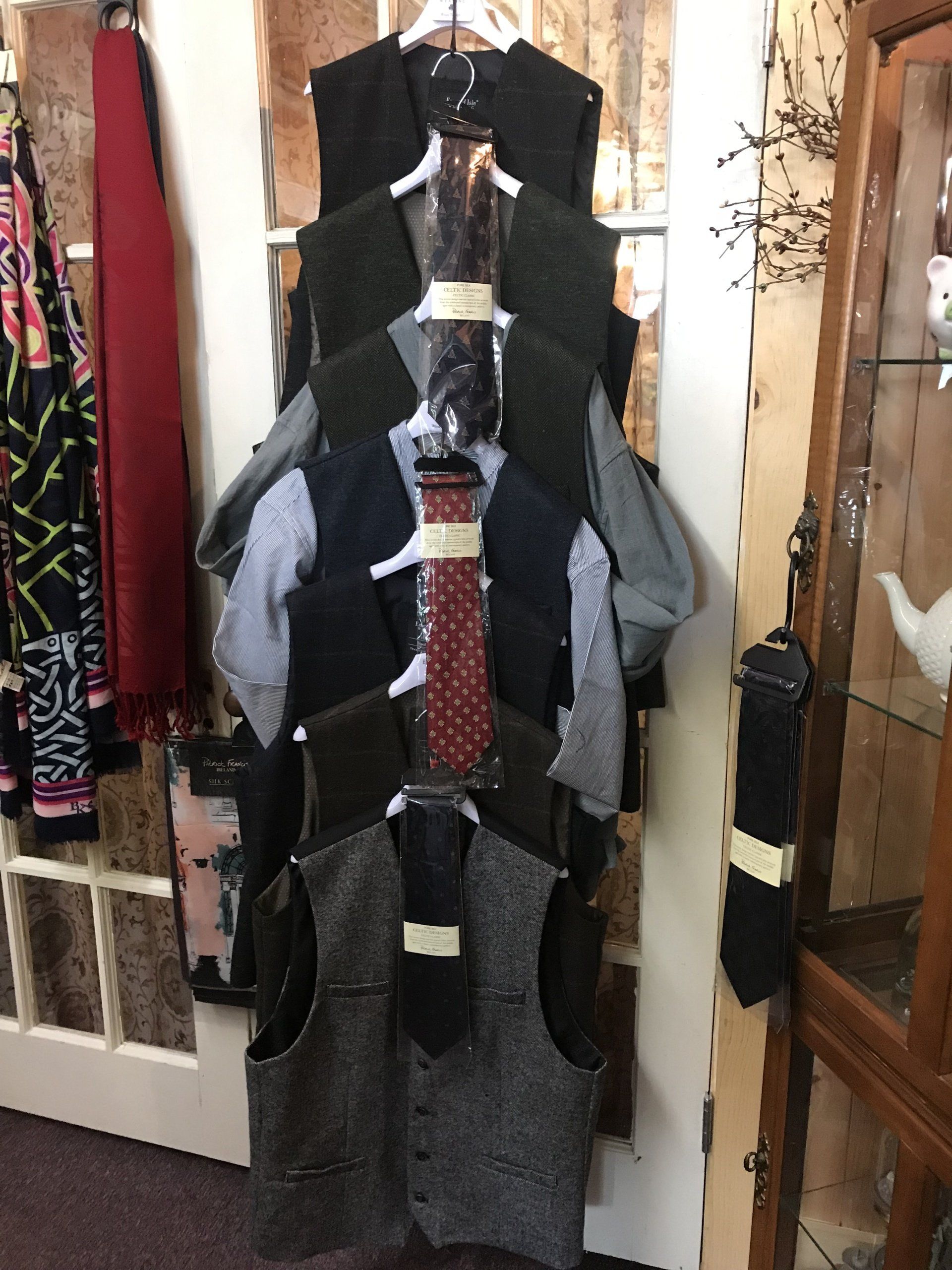 a bunch of vests and ties are hanging on a rack