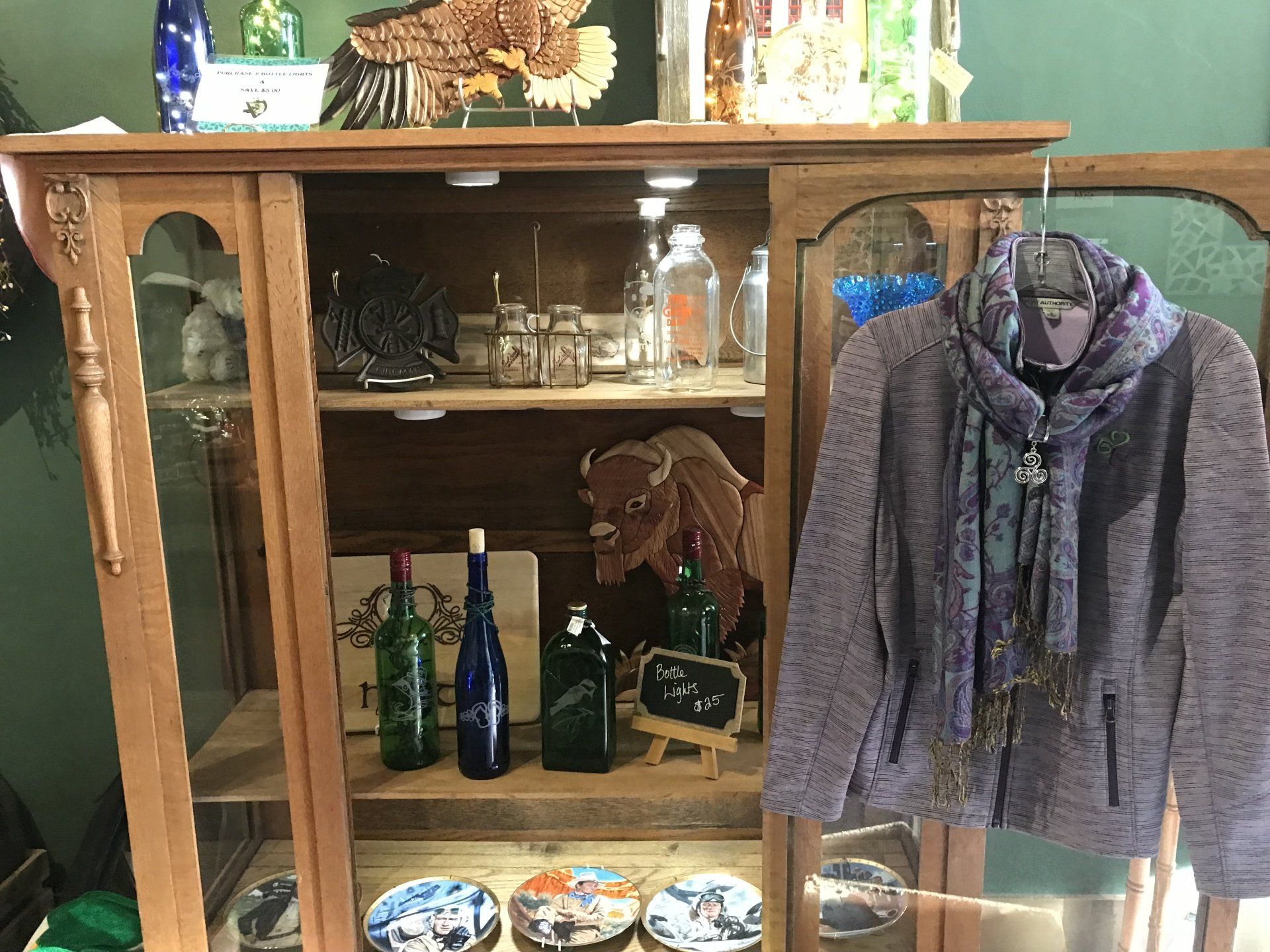 a purple jacket is hanging on a hanger in front of a glass cabinet filled with bottles and plates .