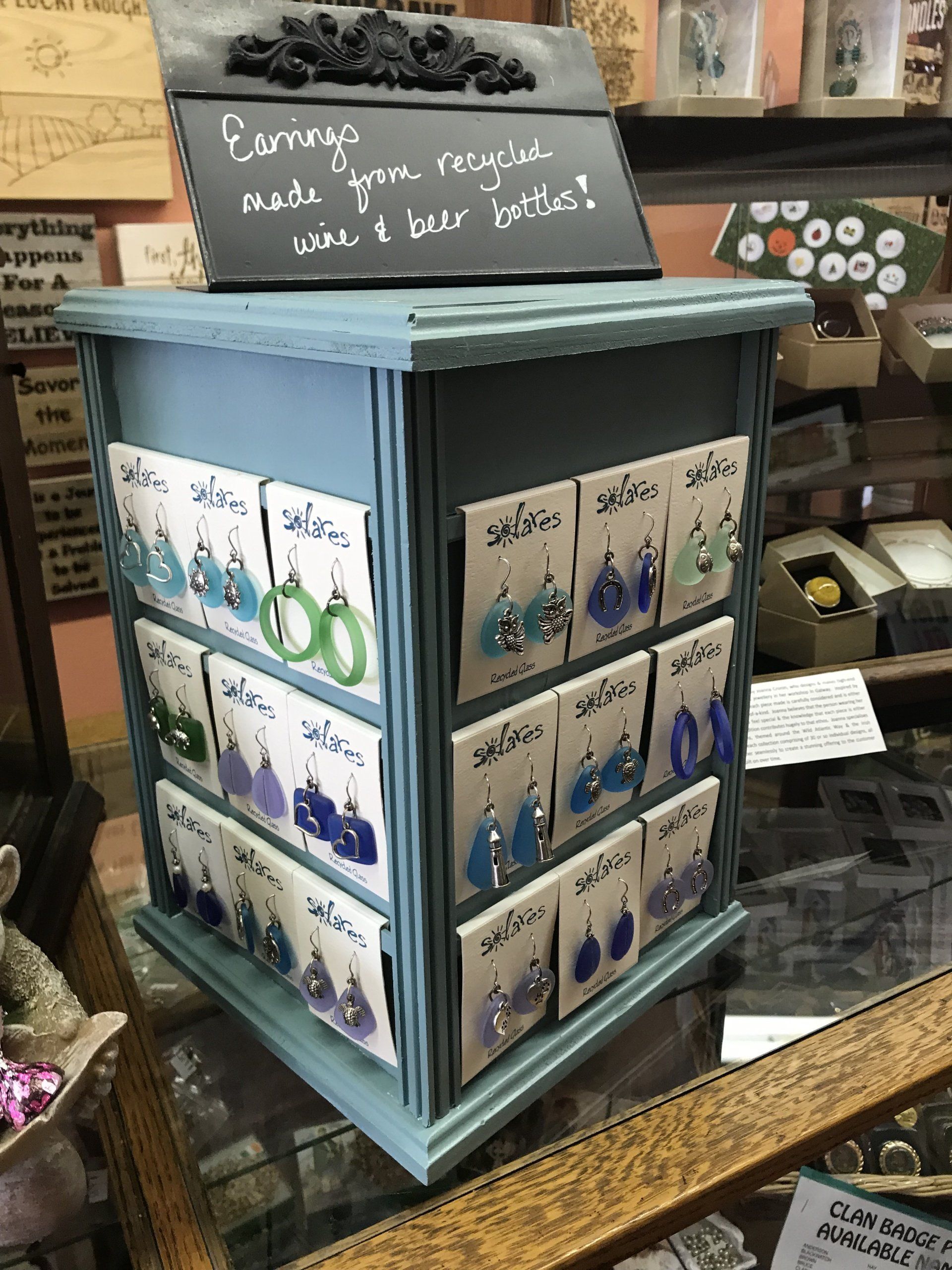 a display case filled with earrings and a sign that says earrings made from recycled glass and beer bottles .