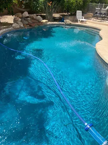 Swimming pool with a blue vacuum hose; blue water, sunny day.