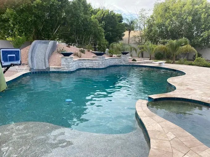 Swimming pool with slide, basketball hoop, and water features, surrounded by landscaping.