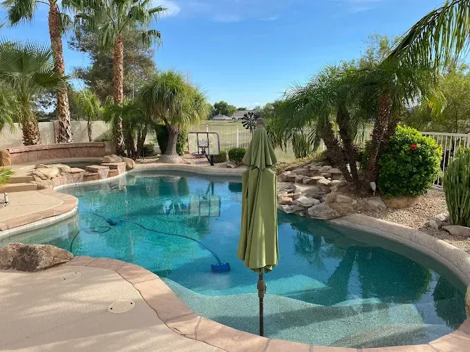 Swimming pool with turquoise water surrounded by rocks, palm trees, and patio.