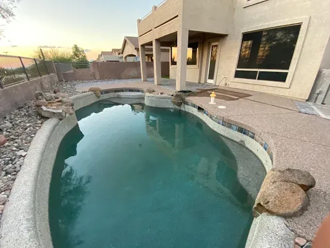 A backyard pool with stone features and a house in the background. The water is a light green color.