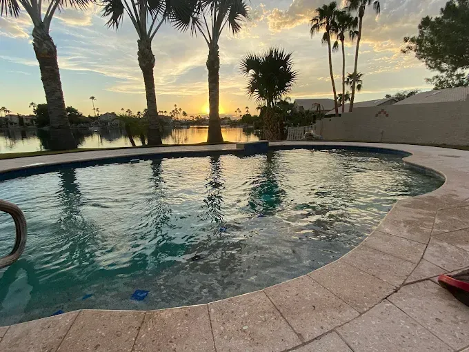 Pool at sunset, water reflecting sky with palm trees and a lake in background.