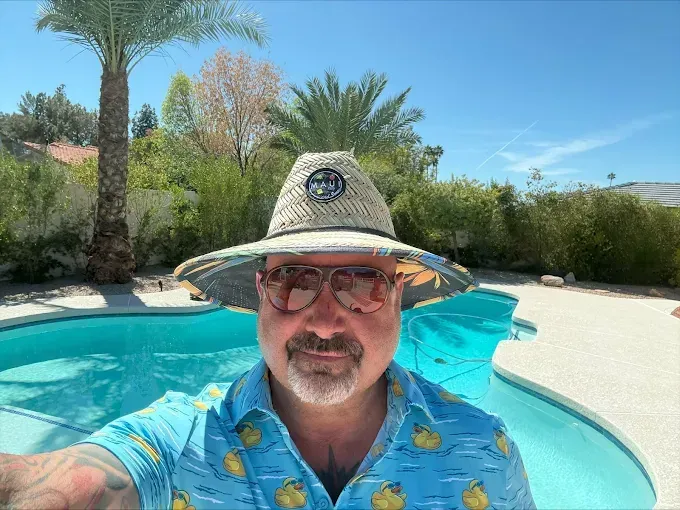 Man wearing hat and sunglasses by pool on sunny day.