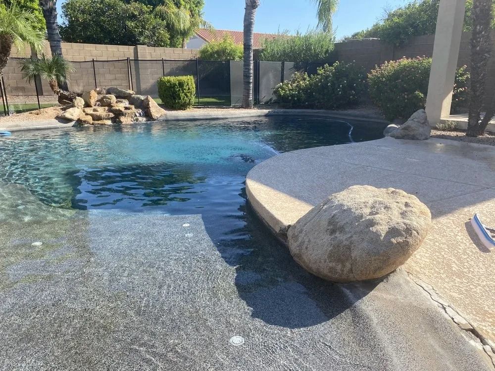 Pool with rock features, surrounded by concrete and landscaping.