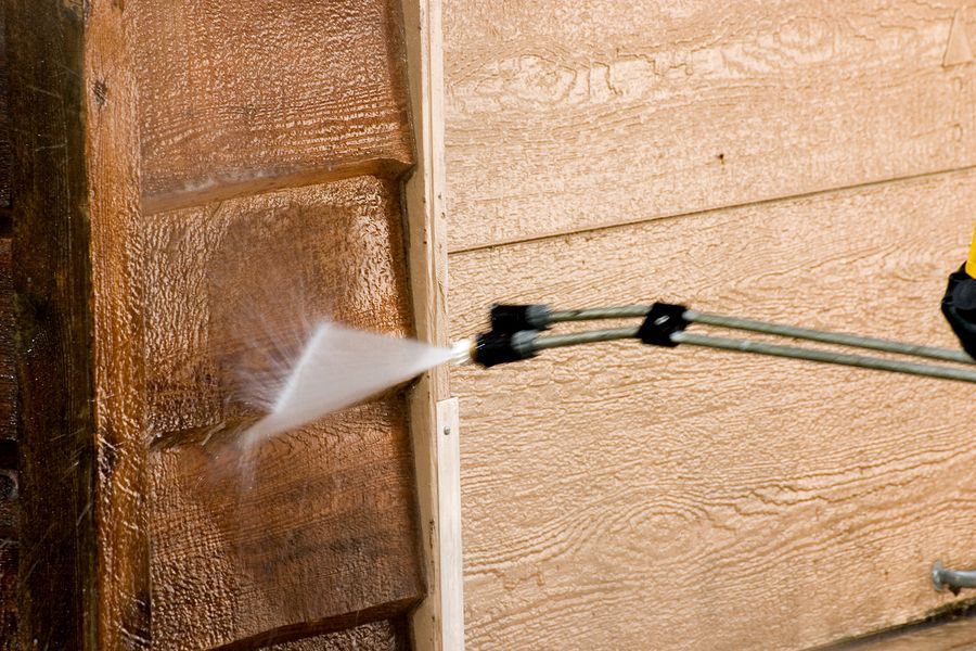 Man pressure washing wood siding, removing dirt.