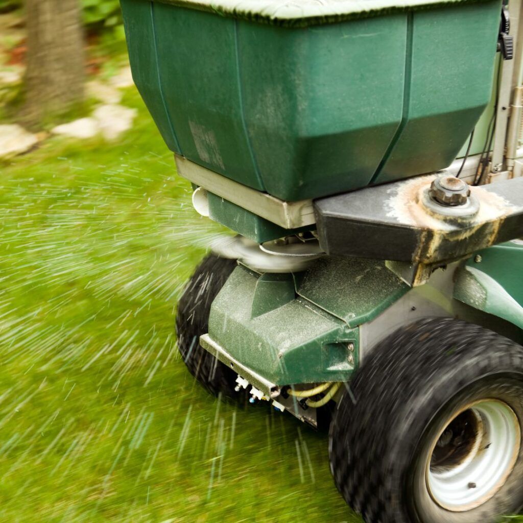 A green lawn mower is spraying fertilizer on a lush green lawn