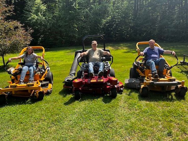 Amanda Bidwell, Robert Bidwell, David Bidwell
Three people on riding lawn mowers in a sunny yard, surrounded by green grass.