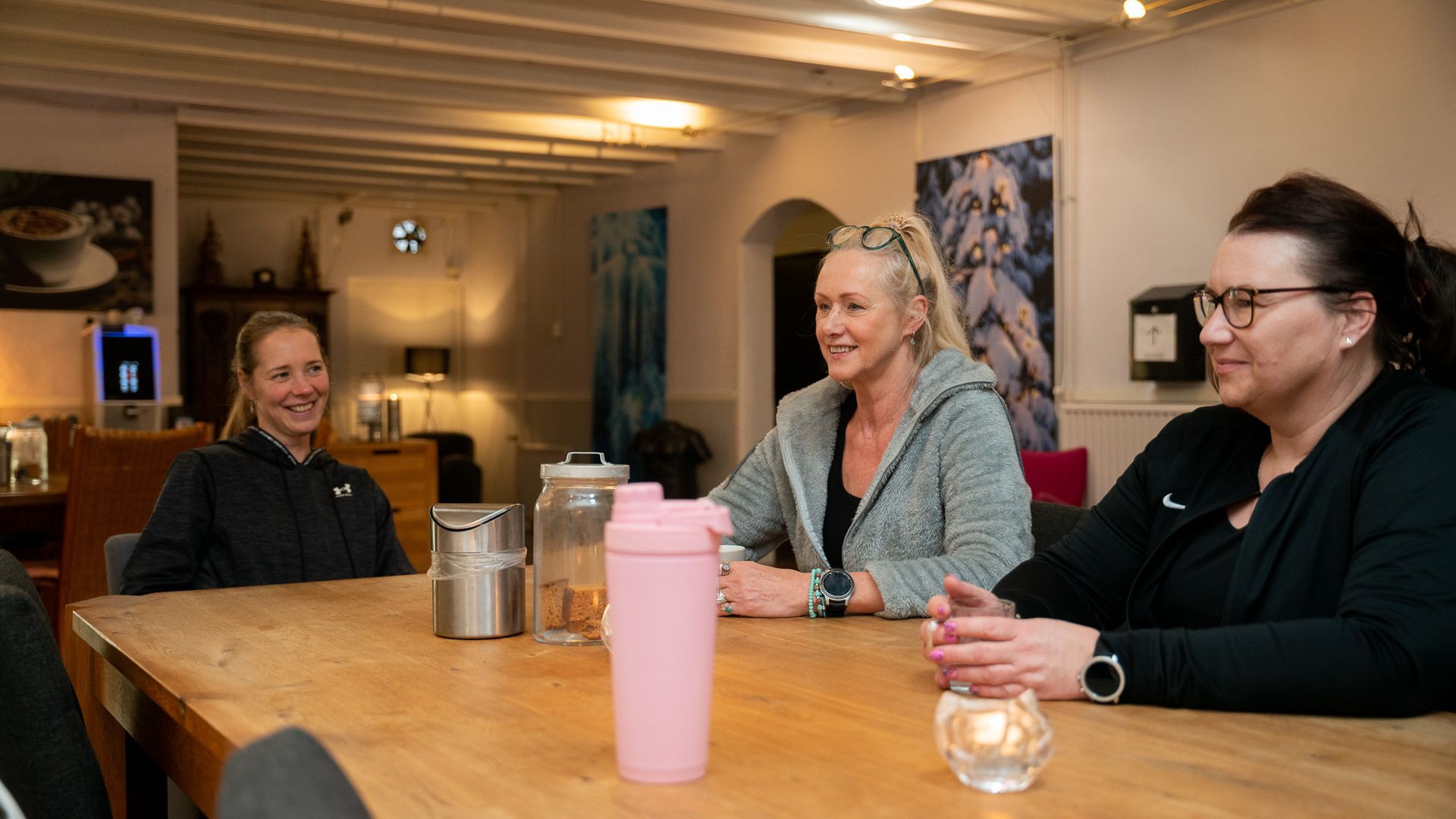 Drie vrouwen zitten aan een tafel in een kamer en praten met elkaar.