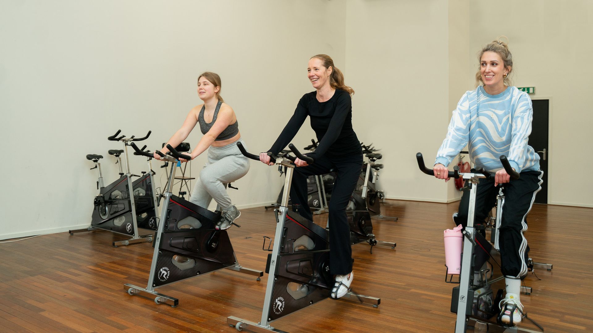 Drie vrouwen zijn aan het fietsen op hometrainers in een sportschool.
