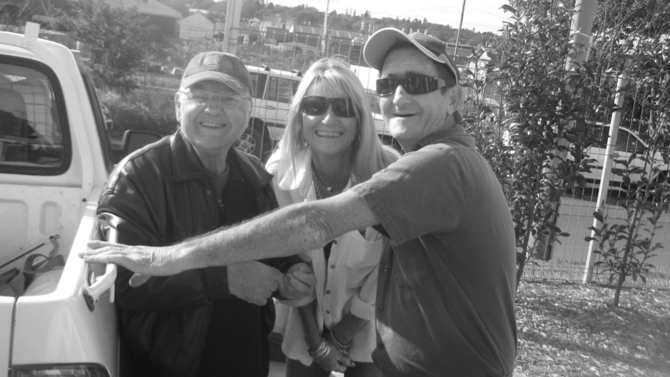 Two males and a female standing next to a ute smiling 