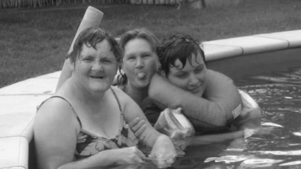 Three people sitting in a swimming pool against the edge 