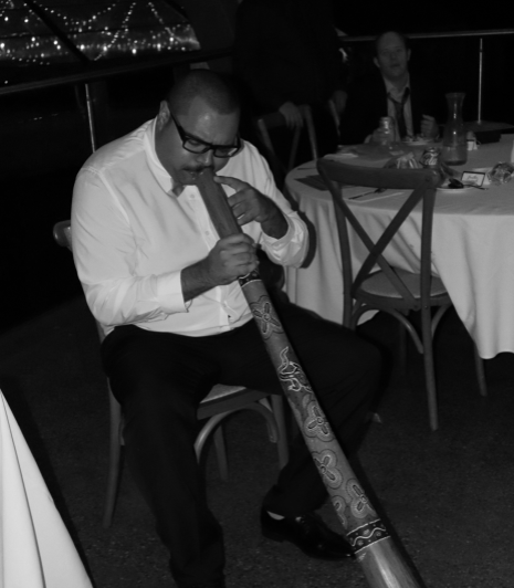 Male sitting at a table playing the didgeridoo 