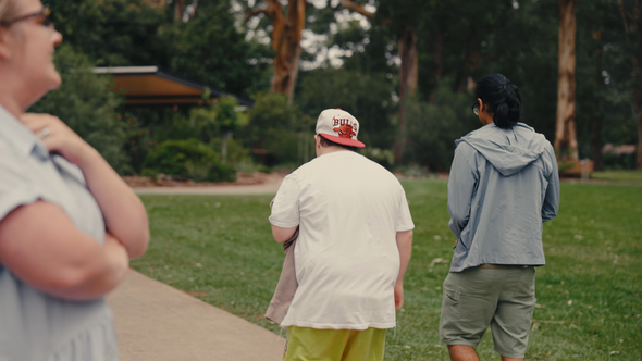 Client and support worker walking into the distance along a paved path in the park