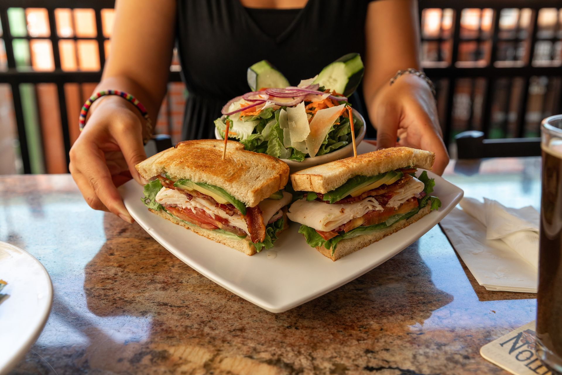 A woman is holding a plate of sandwiches and a salad.