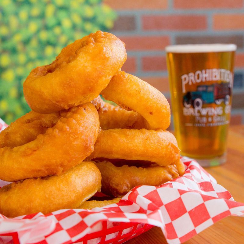 A stack of onion rings next to a glass that says prohibition brewing