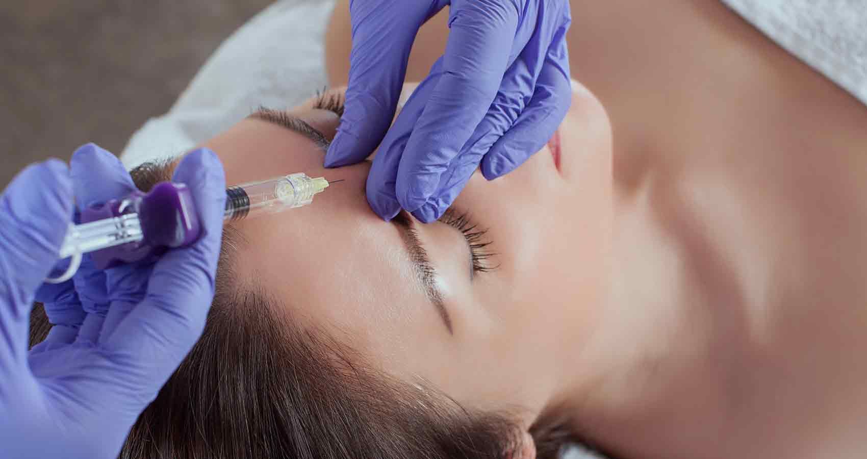 A woman is getting a botox injection in her forehead.