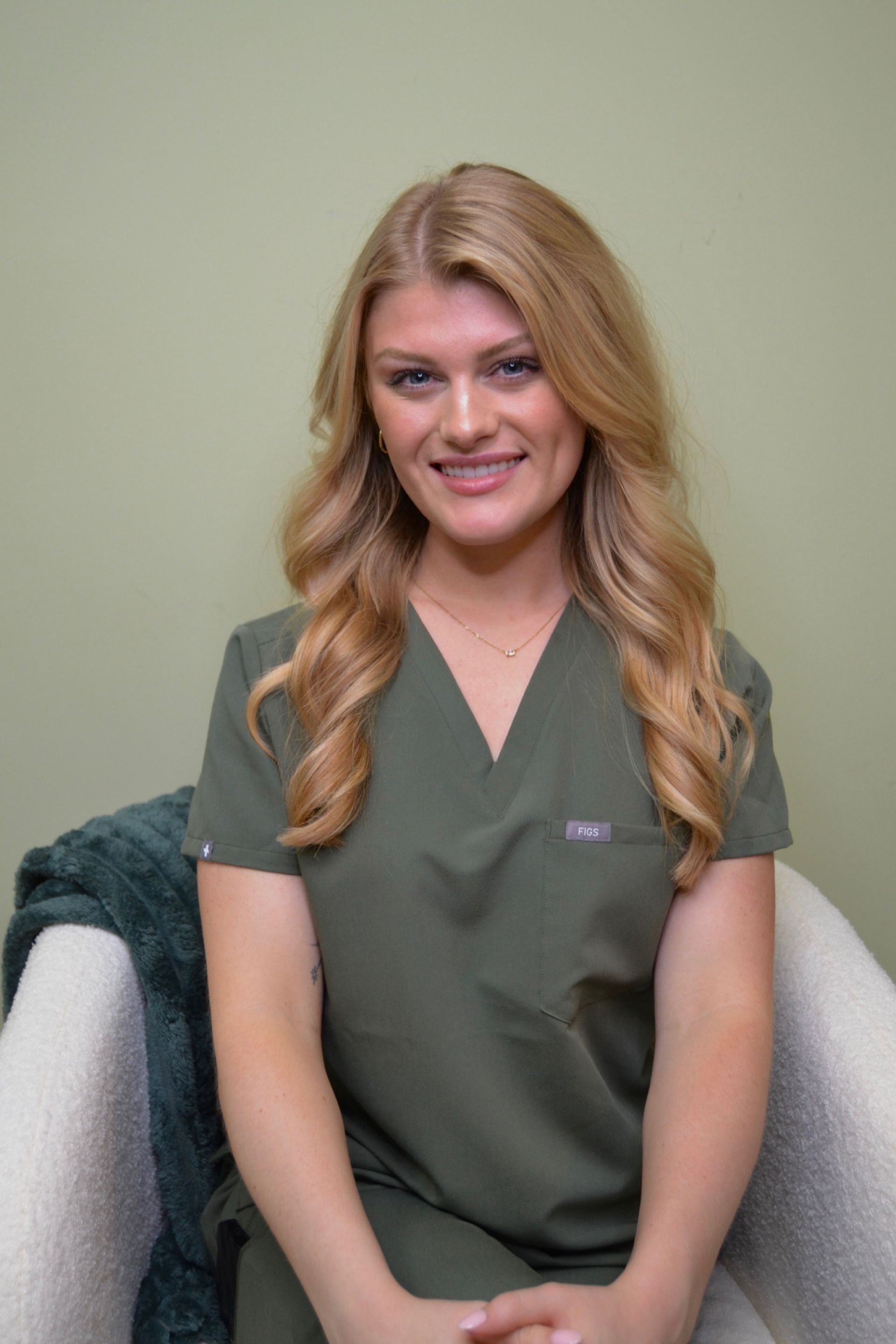 A woman in a green scrub top is sitting in a chair.