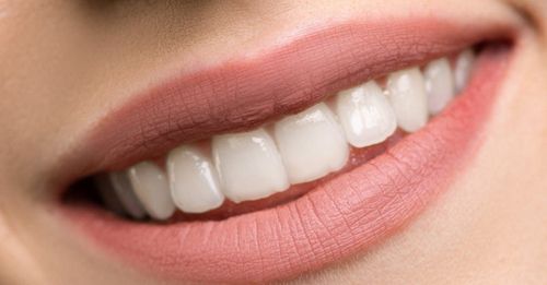 A close up of a woman 's mouth with white teeth and pink lips.