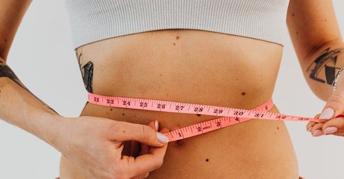 A woman is measuring her waist with a tape measure.