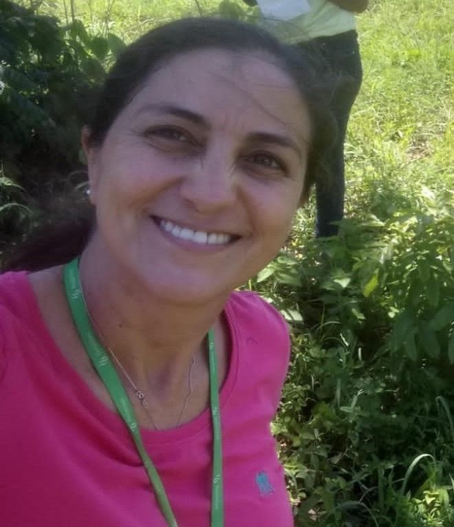 Uma mulher de camisa rosa está sorrindo em um campo.