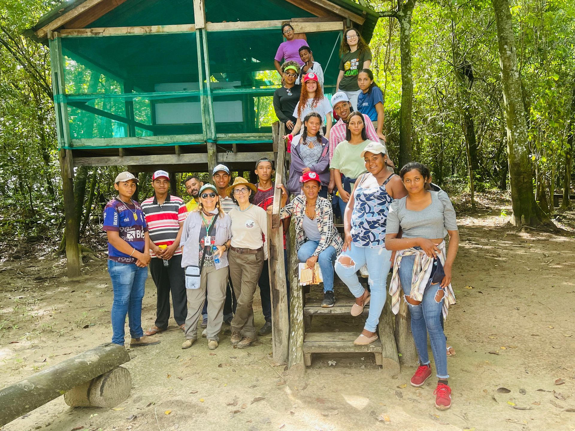 Um grupo de pessoas está posando para uma foto em frente a uma cabana na floresta.
