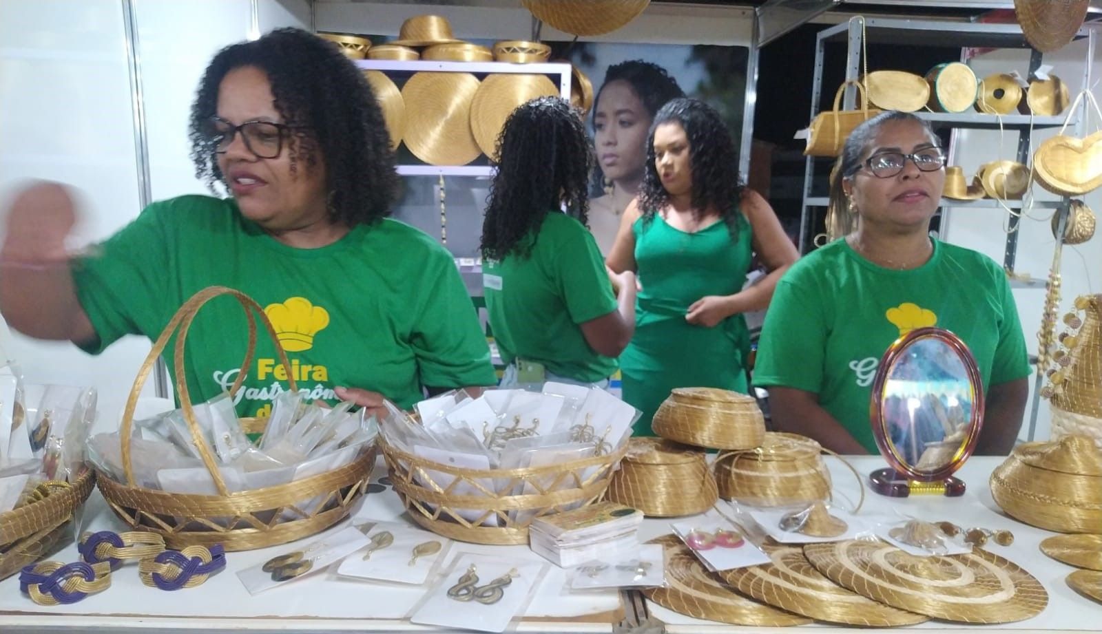 Um grupo de mulheres de camisas verdes estão sentadas à mesa com cestas.