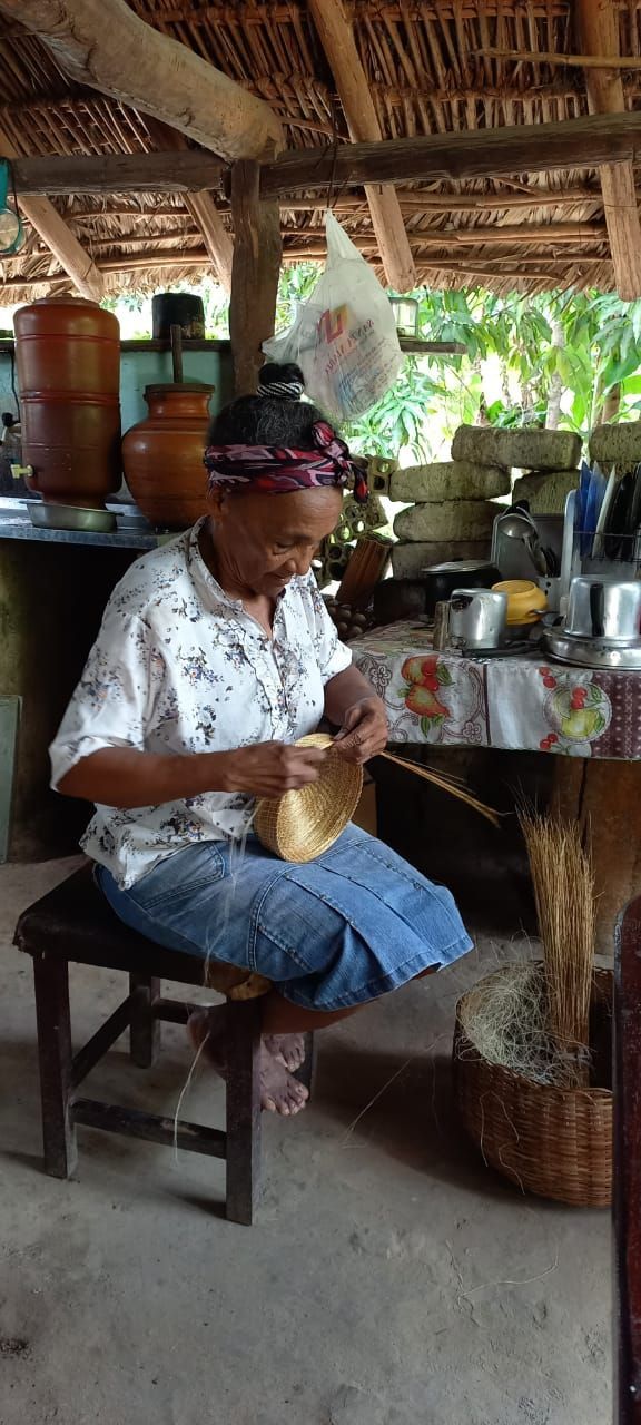 Uma mulher está sentada em um banquinho na cozinha fazendo uma cesta.