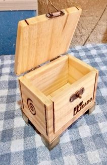 Uma pequena caixa de madeira com a tampa aberta está sobre uma toalha de mesa xadrez.