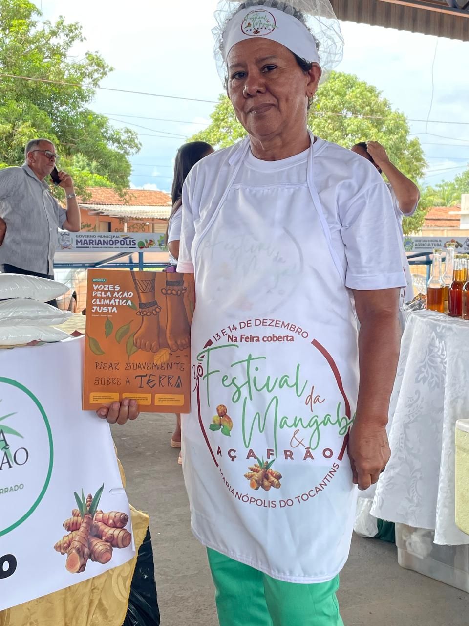 Uma mulher de avental está parada em frente a uma mesa segurando uma placa.