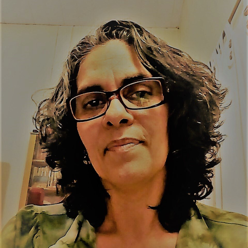Uma mulher de óculos e camisa verde olha para a câmera