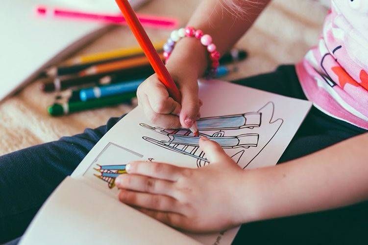 A little girl is sitting on the floor drawing with a pencil.