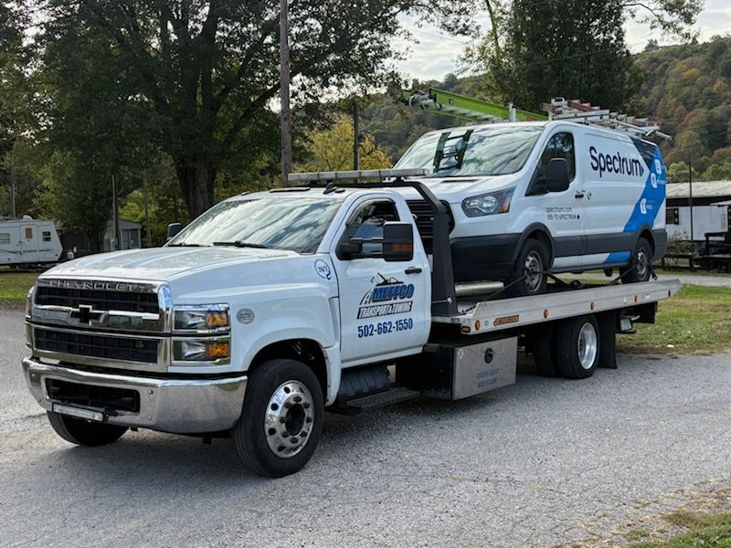 White tow truck carrying a Spectrum van on a flatbed trailer.