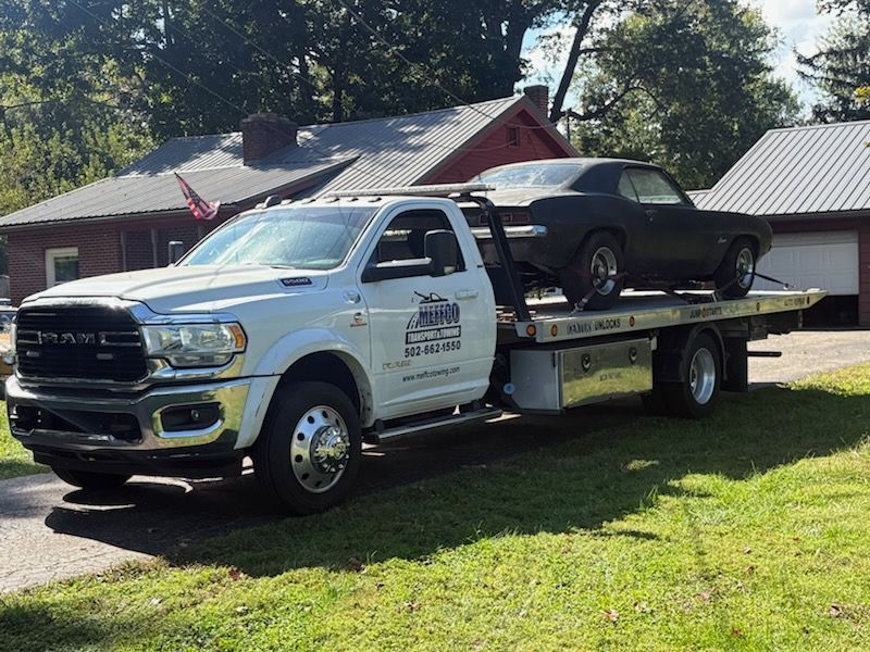 White tow truck carrying a black classic car on a sunny day.
