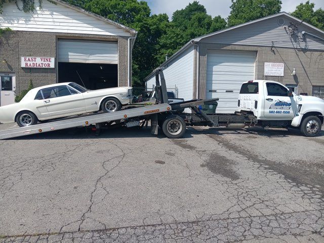 White classic car on a tow truck in front of a repair shop on a sunny day.