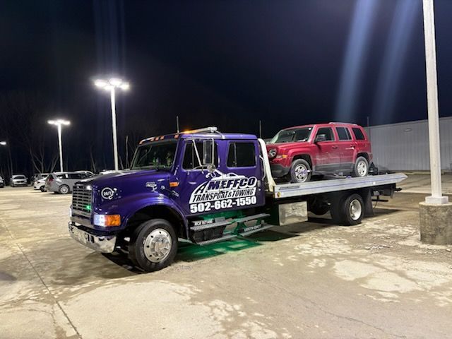 Tow truck with red SUV loaded in parking lot at night.