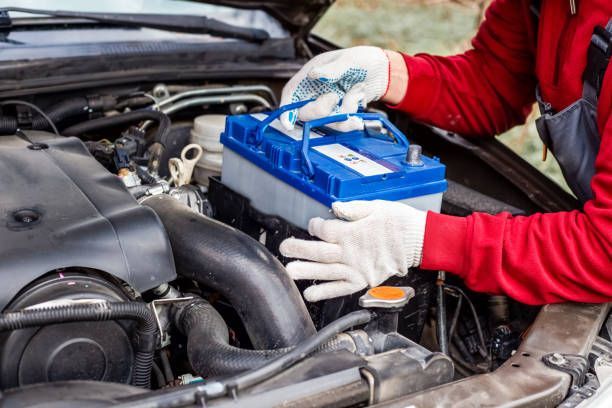 Person wearing gloves replacing a car battery under the hood.