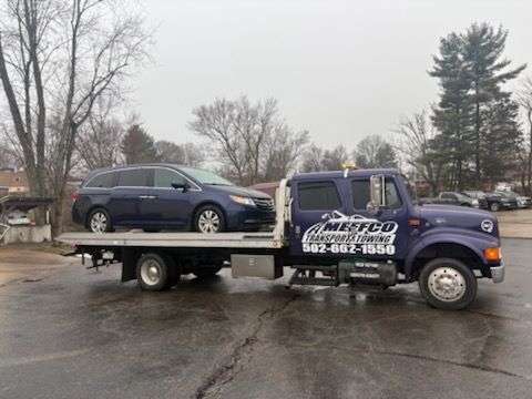 A blue minivan is being towed on a purple tow truck with the 