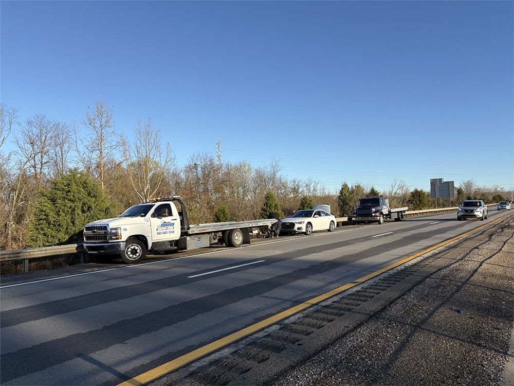 Several tow trucks parked on a highway shoulder, one carrying a white sports car.
