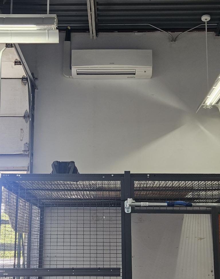 An air conditioning unit on a light gray wall above a black cage, indoors.